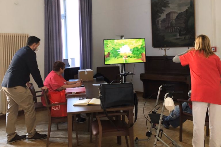 Anwendungsszenario in einer Pflegeeinrichtung: Eine ältere Person interagiert im Sitzen durch Armbewegungen mit dem AR-Spiel Apfelernte auf einem großen Bildschirm.